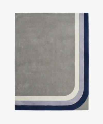 Full top-down product isolated shot of the rectangular Halo Verge area rug, featuring a large minimalist grey field bordered by retro mid-century curved corner bands in cream, lavender purple, and deep navy blue.
