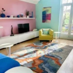 Wide perspective interior lifestyle shot of the Landform Drift abstract area rug styled in a modern living room with a yellow armchair and grey sofa.