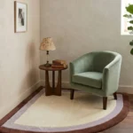 Wide perspective interior lifestyle shot of the Lilac Horizon corner rug styled on dark wood flooring underneath a sage green velvet armchair.