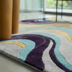 Low angle floor-level close-up showcasing the plush hand-tufted pile variations, precision carving lines, and dimensional deep purple and aqua swirls of the Luma River rug.