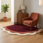 Wide perspective lifestyle room view showing the Lunar Arc scalloped corner rug styled on light wooden flooring with a rust-colored armchair.