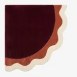 Full top-down product isolated shot of the uniquely shaped Lunar Arc scalloped corner rug featuring concentric wavy bands of burgundy, terracotta, and cream.