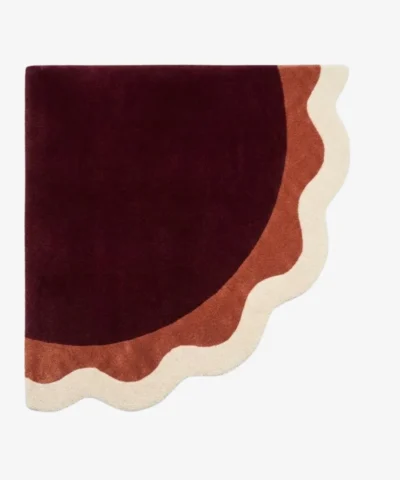 Full top-down product isolated shot of the uniquely shaped Lunar Arc scalloped corner rug featuring concentric wavy bands of burgundy, terracotta, and cream.