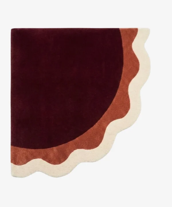 Full top-down product isolated shot of the uniquely shaped Lunar Arc scalloped corner rug featuring concentric wavy bands of burgundy, terracotta, and cream.