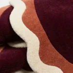 Close-up macro photograph highlighting the thick wool material texture and stacked scalloped edges of the folded Lunar Arc rug.