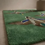Low side-angle perspective shot showing the smooth pile texture and corner profile of the green duck-themed rug.