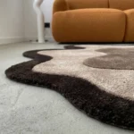 Low-angle side view of the Mocha Drift rug on a light concrete floor, emphasizing the high-pile depth, uniform thickness, and clean carved borders of the hand-tufted fibers.