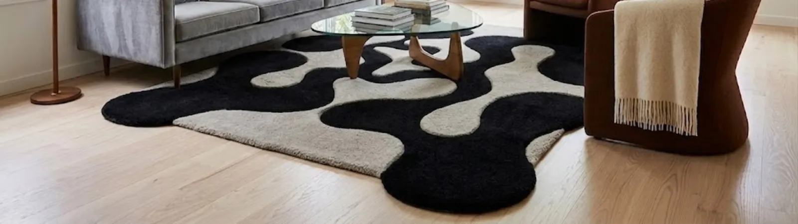 Wide low angle perspective of a modern abstract rug featuring an irregular wavy puzzle border in black and off-white blocks styled in a living room.