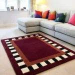 Perspective interior shot of the Montero Border rug styled in a modern living room with a light gray sofa and colorful accent pillows.