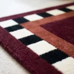 Close-up macro photograph highlighting the thick, plush wool material texture and sharp checkered border details of the Montero Border rug.