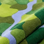 Close-up macro photograph highlighting the premium wool material texture, tight loop construction, and vibrant solid color blocks of the folded Mossbrook rug.