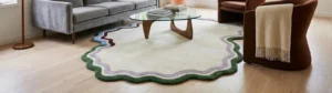 Wide perspective interior lifestyle shot of a large, cream-colored irregular odd-shaped rug featuring a multi-colored wavy scalloped border styled in a modern living room under a glass coffee table.