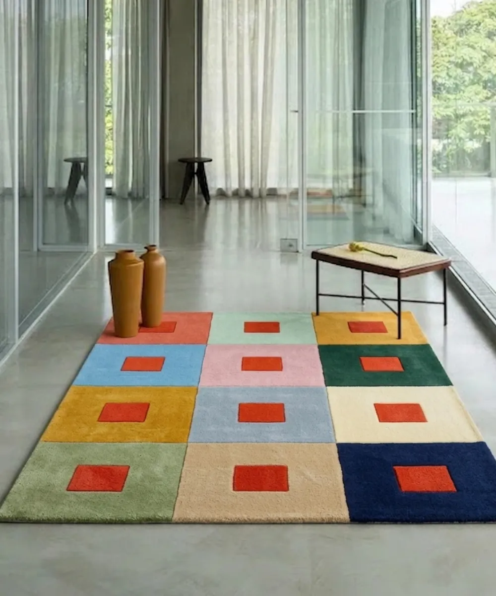 Wide perspective interior lifestyle shot of the Pixel Palette colorful grid rug styled on a sleek polished concrete floor in a modern minimalist space with large glass walls.