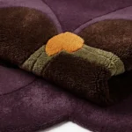 Close-up macro photograph highlighting the thick wool material texture, dense pile tracking, and rich jewel-toned palette of the folded Plum Orchid floral rug.
