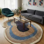 Wide perspective interior lifestyle shot of the Sediment abstract organic rug styled in a minimalist living room with a grey sofa and teal armchair.