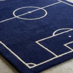 Low angle close-up floor perspective showcasing the plush hand-tufted pile and crisp white pitch lines of the soccer field area rug.