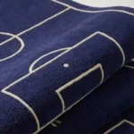 Close-up macro photograph highlighting the premium wool material texture and dense pile construction of the folded soccer field rug.