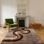 Wide perspective interior lifestyle view of the Walnut Current retro wave rug styled on a classic herringbone hardwood floor in an elegant room featuring a white fireplace mantel and a vibrant green accent chair.