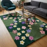 Wide perspective interior lifestyle shot of the Wildflower Meadow floral rug styled on light wood flooring in a modern living room under a glass coffee table with a grey sofa and teal accent chair.