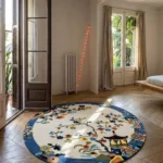 An interior lifestyle shot of the Celadon round rug styled on hardwood flooring in a sunlit room, complemented by neutral curtains and simple minimalist decor.