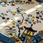 An angled perspective shot of the Celadon round rug, highlighting the detailed tufted craftsmanship of the oriental pagoda and floral landscape design.