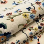 A macro close-up of the folded Celadon rug, focusing on the dense, premium wool pile and the vivid, detailed embroidery of the floral branches and oriental motifs.