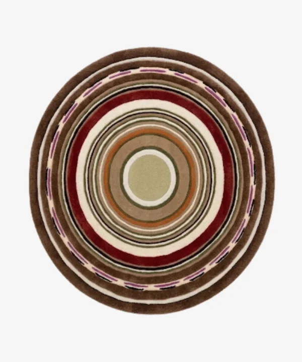 A top-down studio product photograph of a round area rug featuring concentric circular patterns in rich tones of chestnut, deep red, cream, and purple, displayed on a clean background.