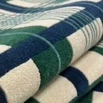 A macro close-up of the folded Evergreen Plaid rug, focusing on the dense, premium wool pile and the detailed grid construction of the green, blue, and off-white plaid design.