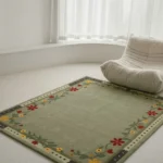 A full angled view of the rectangular Florivert green rug with a floral vine border, styled in a minimalist bright white room beside a cozy tufted floor sofa.