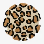 Full top-down product isolated shot of the round Leora area rug, featuring an organic, hand-carved wavy perimeter and a classic animal rosette pattern with camel brown and black leopard spots on an off-white background field.
