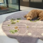 An angled perspective of the Liora Moss rug in a bright room with a dog resting on it, highlighting the rug's unique organic shape and multi-colored cellular design.