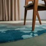 Angle view of the handmade Marina Wave tufted rug showcasing its unique organic contours, ocean gradient tones, and wooden chair legs.