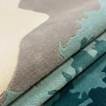 Close-up of the plush tufted pile texture, coastal color transitions, and soft cream, grey, and teal tones on the Marina Wave rug.