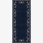 A top-down studio product photograph of a rectangular navy blue runner rug featuring a decorative beige scalloped border and intricate floral vine motifs.