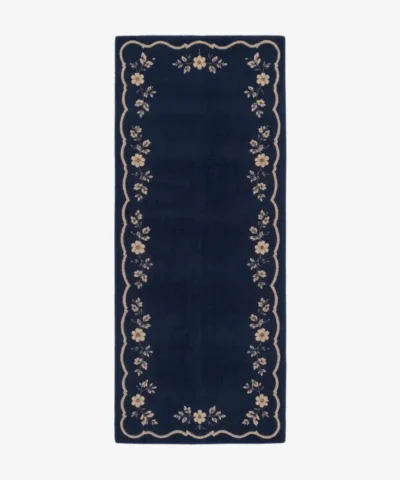 A top-down studio product photograph of a rectangular navy blue runner rug featuring a decorative beige scalloped border and intricate floral vine motifs.