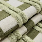 Close-up macro photograph highlighting the distinct high-low pile variations, shaggy tufted horizontal ribbon tracks, and dense wool construction of the folded Moss Interlace area rug.