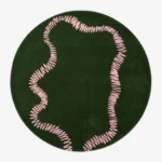An interior lifestyle shot of a round green area rug with a pink squiggly pattern, styled on wooden flooring in a room with pink and light blue walls and a yellow armchair.
