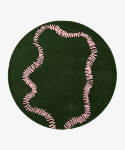 An interior lifestyle shot of a round green area rug with a pink squiggly pattern, styled on wooden flooring in a room with pink and light blue walls and a yellow armchair.