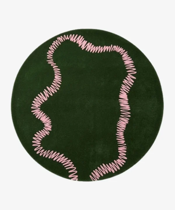 An interior lifestyle shot of a round green area rug with a pink squiggly pattern, styled on wooden flooring in a room with pink and light blue walls and a yellow armchair.