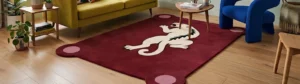 An interior lifestyle shot of a deep red rectangular area rug featuring a stylized white panther motif and rounded scalloped edges, styled on a light hardwood floor in a vibrant living room with a yellow sofa and blue accent chair.