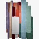 A top-down studio product photograph of the rectangular Prism Verin area rug, featuring an abstract geometric composition with vertical panels in shades of purple, rust, blue, and green.