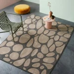 An angled interior lifestyle photograph of a tufted stone pattern area rug styled in a modern room with a green chair and a pink side table.
