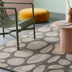A macro close-up of the Riverstone area rug, highlighting the dense tufted wool pile, carved stone outlines, and smooth neutral beige and gray texture.