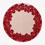 Full top-down product isolated shot of the round Rosara area rug, featuring a dense outer ring pattern of retro stylized poppy flowers in deep crimson red over a solid off-white center field and muted rose pink perimeter.