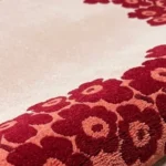 Close-up macro photograph highlighting the premium tufted wool yarn density, shaggy flower petal contours, and crisp color transitions of the rolled Rosara red and off-white rug.