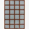 A top-down studio product photograph of the rectangular Russet Ledger area rug, featuring a grid-patterned design with a deep rust-colored border and light blue square inserts.