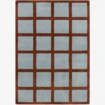 A top-down studio product photograph of the rectangular Russet Ledger area rug, featuring a grid-patterned design with a deep rust-colored border and light blue square inserts.