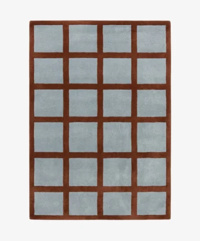 A top-down studio product photograph of the rectangular Russet Ledger area rug, featuring a grid-patterned design with a deep rust-colored border and light blue square inserts.