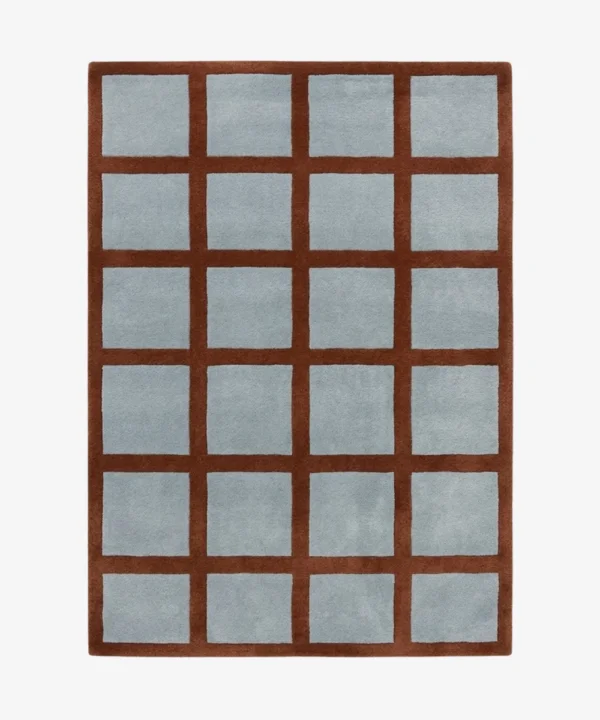 A top-down studio product photograph of the rectangular Russet Ledger area rug, featuring a grid-patterned design with a deep rust-colored border and light blue square inserts.