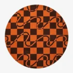 A top-down studio product photograph of a round area rug featuring a geometric orange and dark brown checkerboard pattern overlaid with flowing wavy lines.
